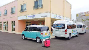 A building with a sign for 'Pine Rent a Car'. There are two white vans parked in front with luggage.