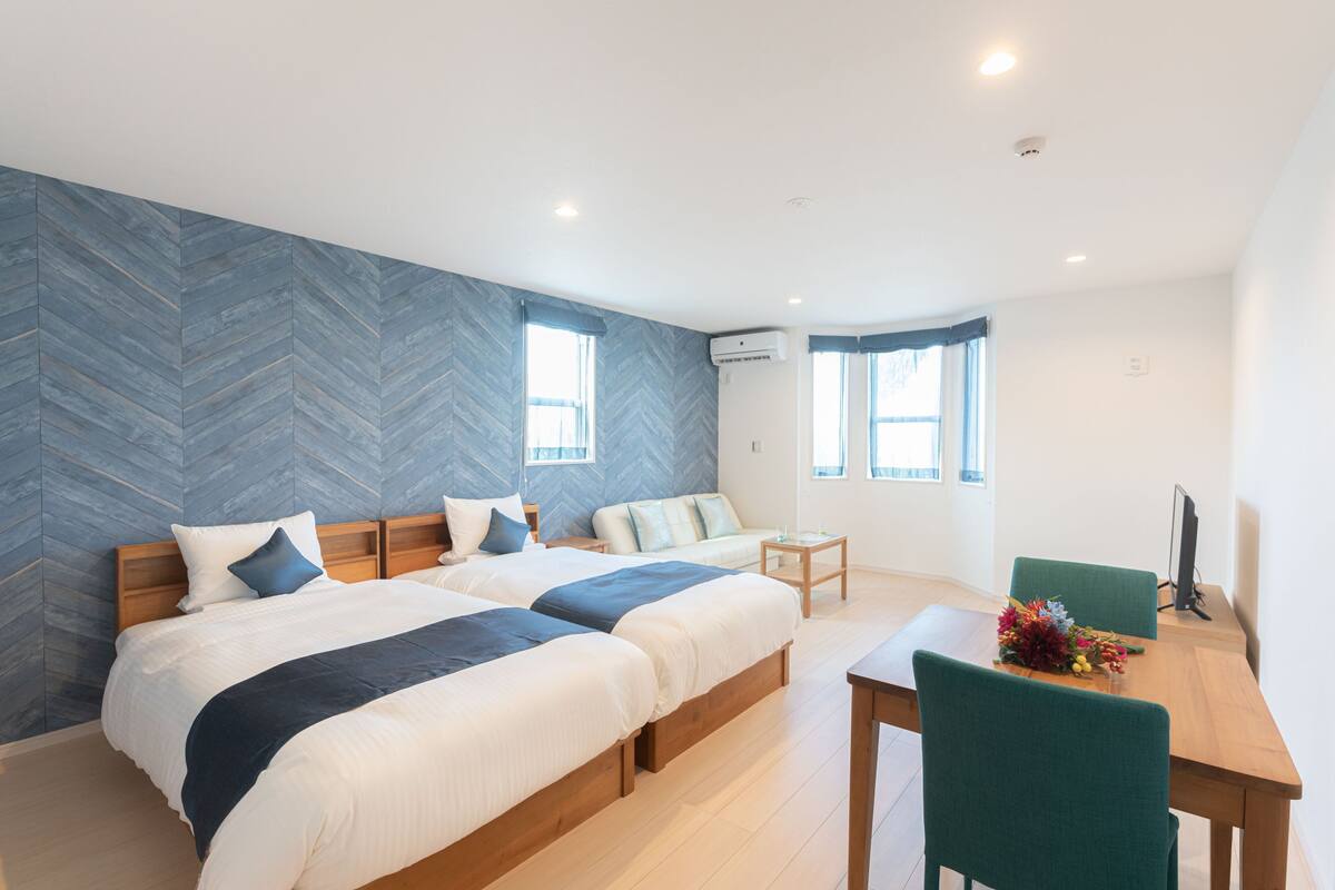 A modern hotel room with two beds, a dining table, and a TV.