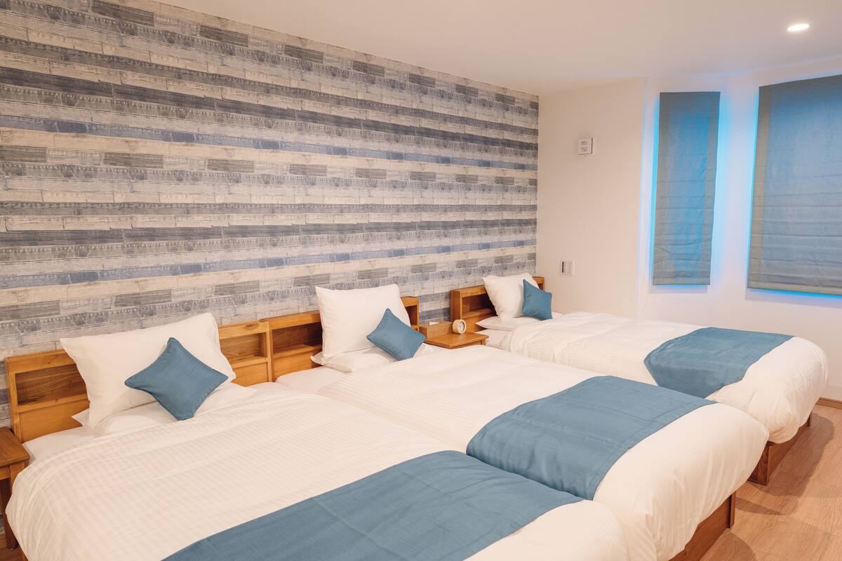 A hotel room with three beds, wooden headboards, and a large textured wall.