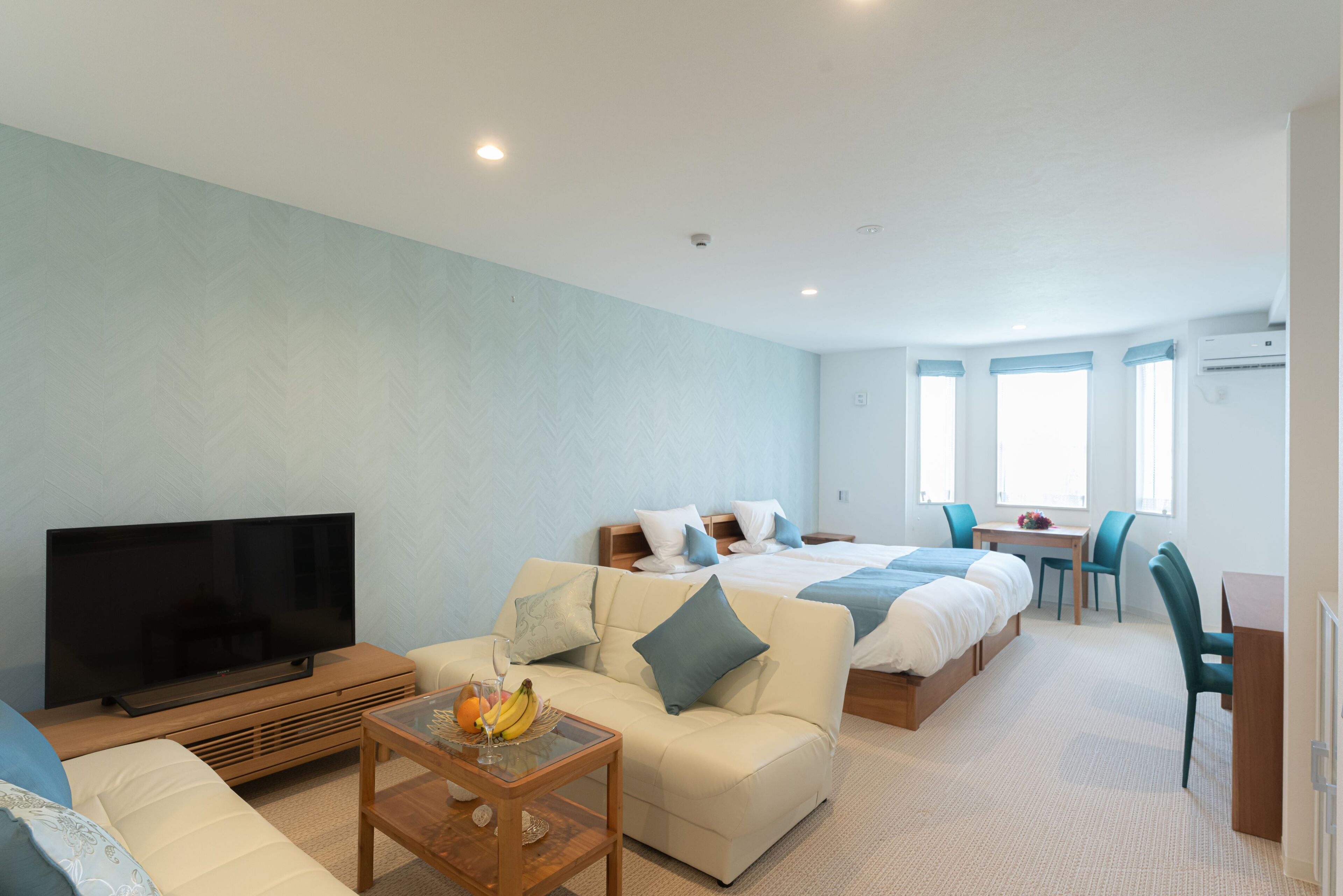A modern hotel room with a large bed, a sofa, a TV, and a dining area.