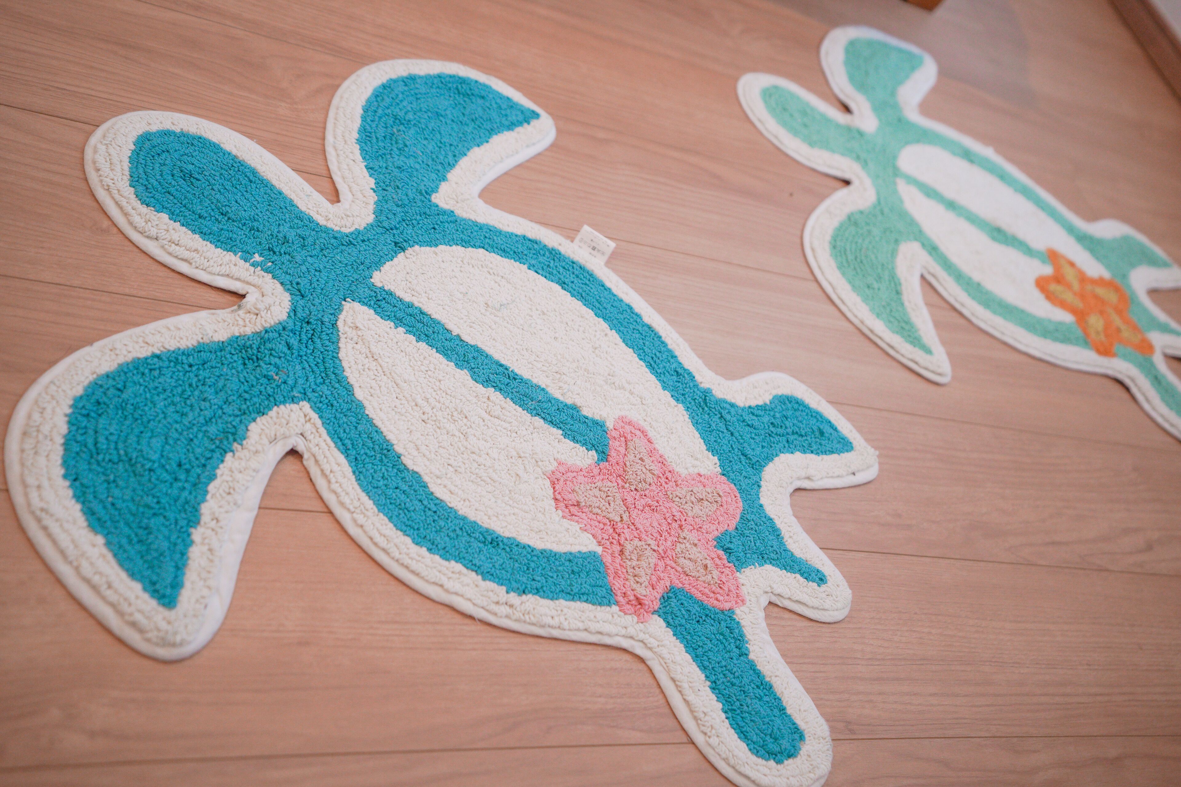 A wooden floor with two large, colorful, crocheted turtle rugs.