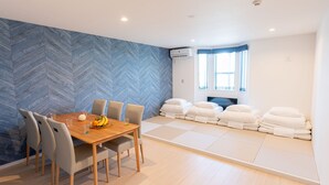 A modern room with a herringbone-patterned wall, a wooden dining table with chairs, a window with curtains, and a stack of white pillows.