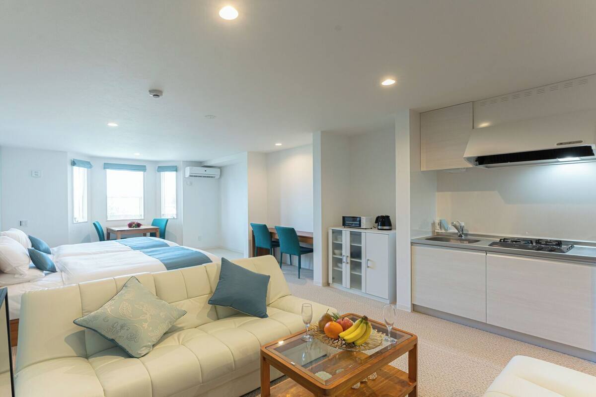 A modern apartment with a bed, sofa, dining area, kitchen, and a small balcony.