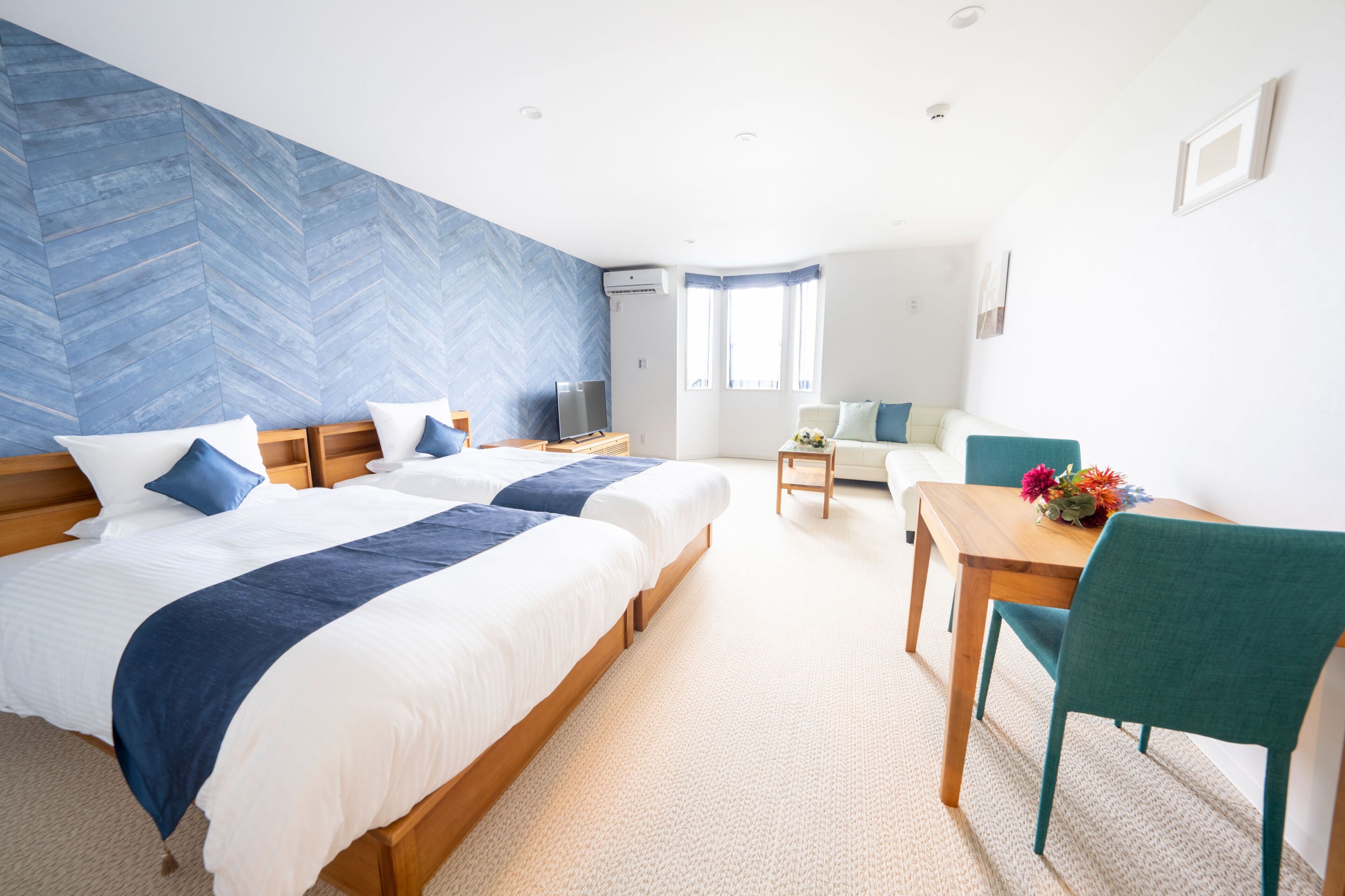 A hotel room with two beds, a desk, a chair, and a sofa.