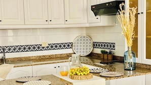 A kitchen with white cabinets, a granite countertop, a black and white patterned backsplash, a black range hood, and a vase with dried plants.