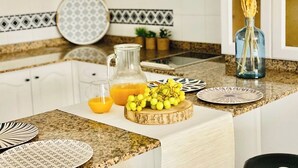 A kitchen counter with a pitcher of orange juice, a glass of orange juice, and a plate of grapes.