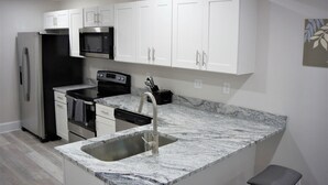 Una cocina moderna con armarios blancos, un refrigerador de acero inoxidable, un microondas, un horno y un lavamanos con encimera de mármol.