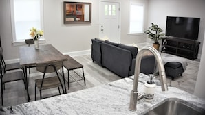 Una cocina moderna con encimera de mármol, lavaplatos integrado y comedor con mesa y sillas de madera.