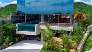 Et moderne hus med stor glasfacade, swimmingpool og frodig beplantning omkring.
