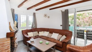 A cozy living room with a brown leather sofa, a wooden coffee table, and a brick fireplace. - Vacation home Ami by Interhome (Calonge)