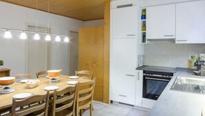 Et moderne køkken med hvide skabe, indbygget ovn og et spiseområde med træstole og et bord.