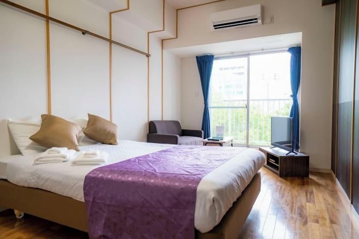 A hotel room with a bed, a chair, a TV, and a window with curtains.