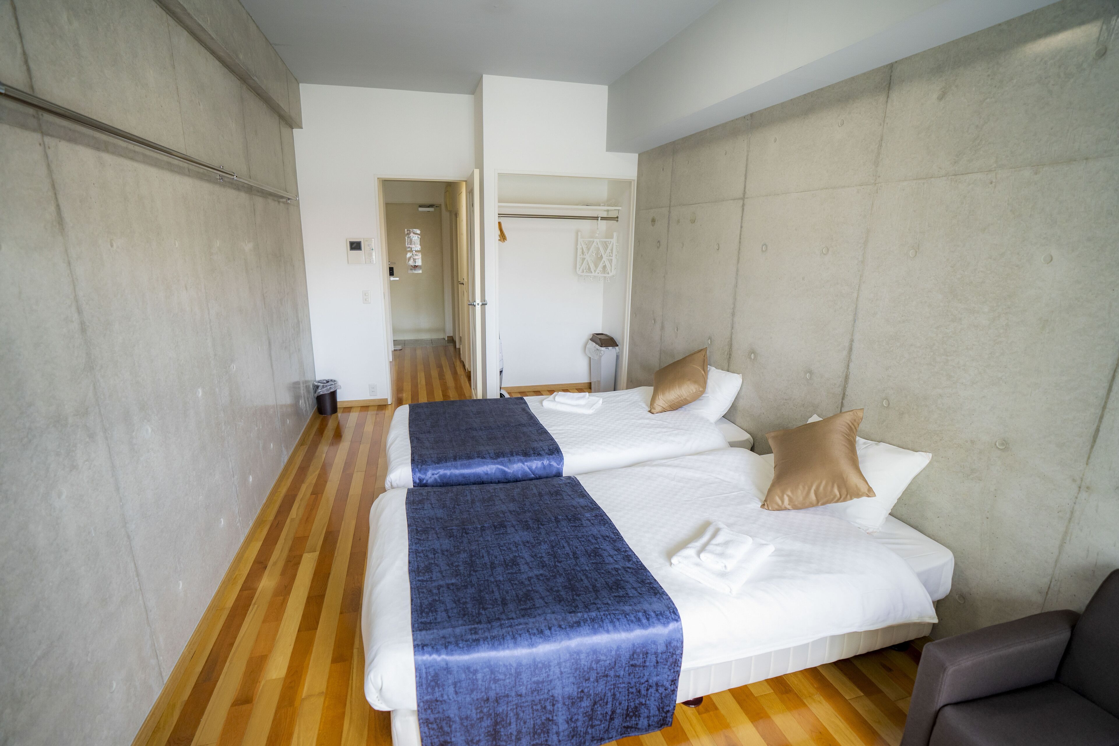 A hotel room with two beds, wooden flooring, and a concrete accent wall.
