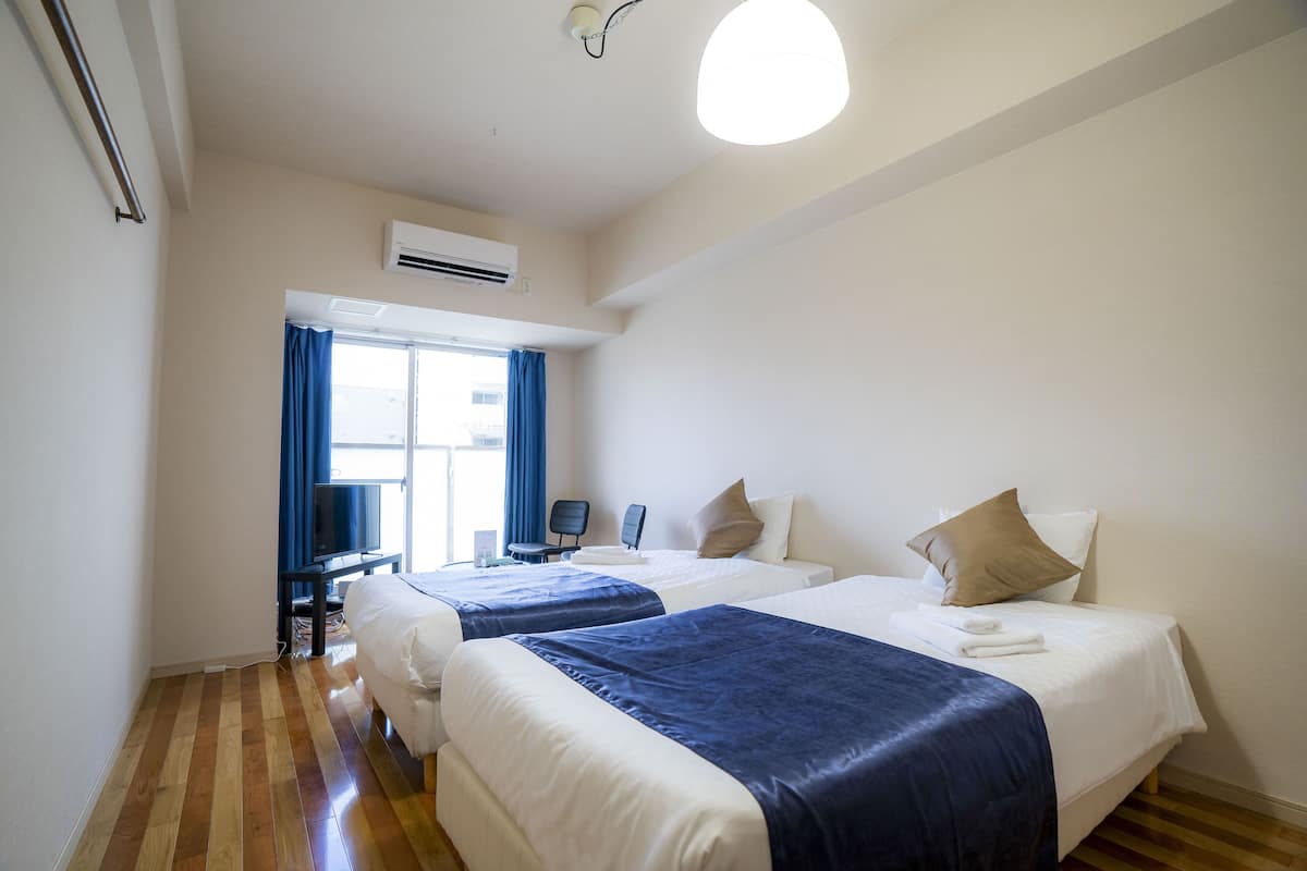 A hotel room with two beds, a TV, a desk, and a window with curtains.