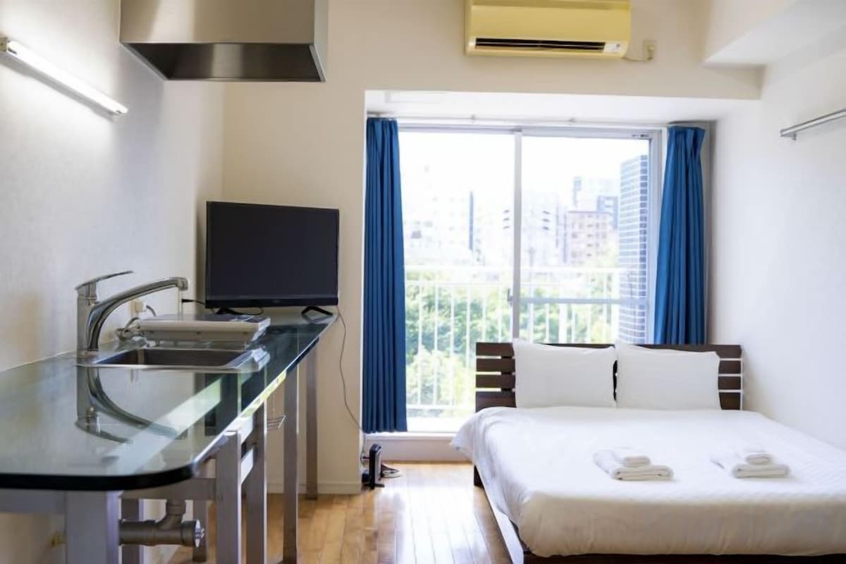 Una camera d'albergo con un letto, una televisione, una finestra con tende e un angolo cottura.
