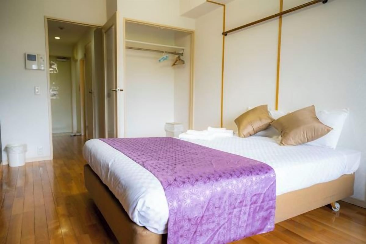 A bedroom with a bed, a bedside table, a wardrobe, and a hallway leading to another room.