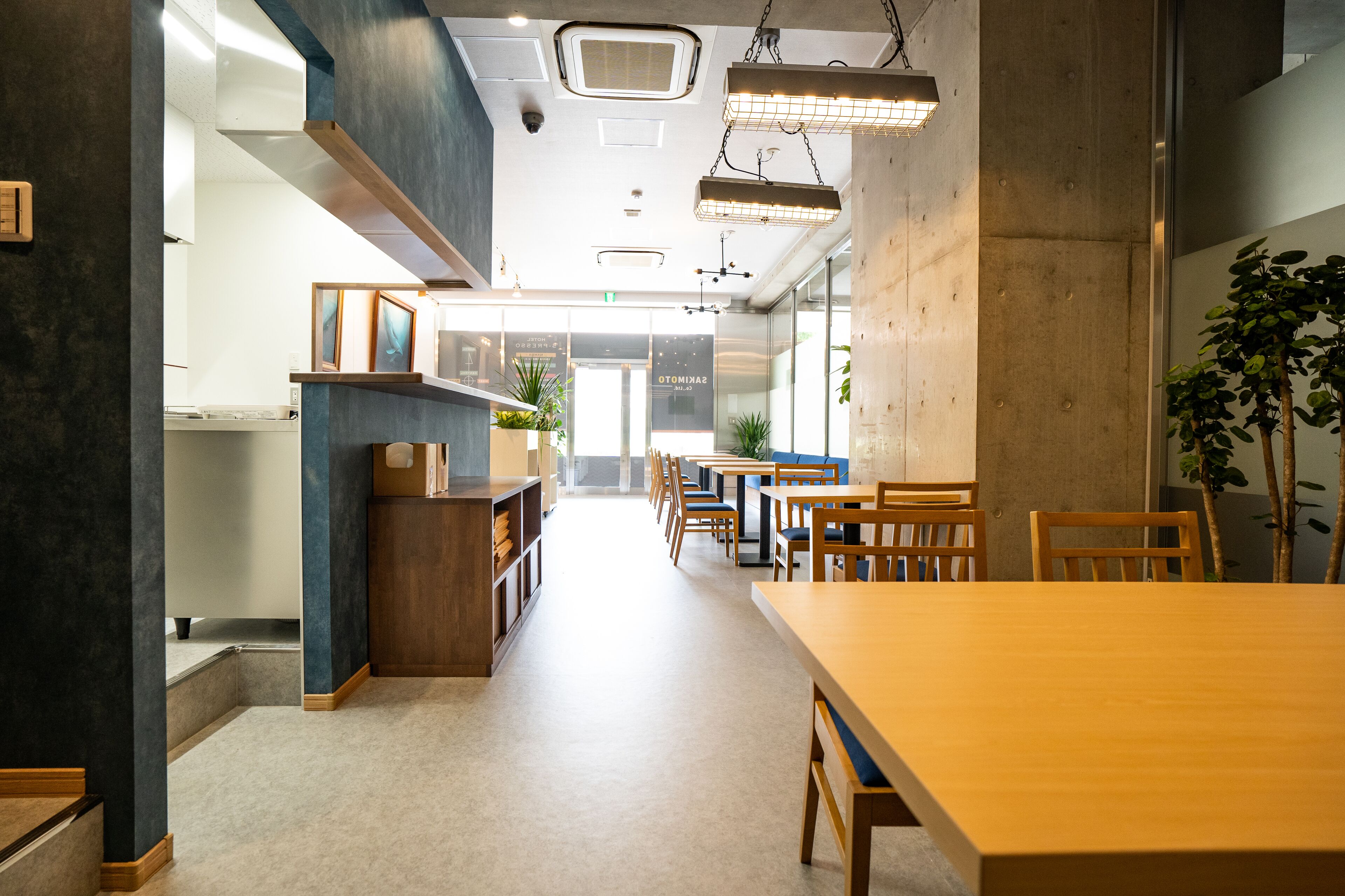 A modern interior with a long wooden table and chairs, a bookshelf, and a plant.
