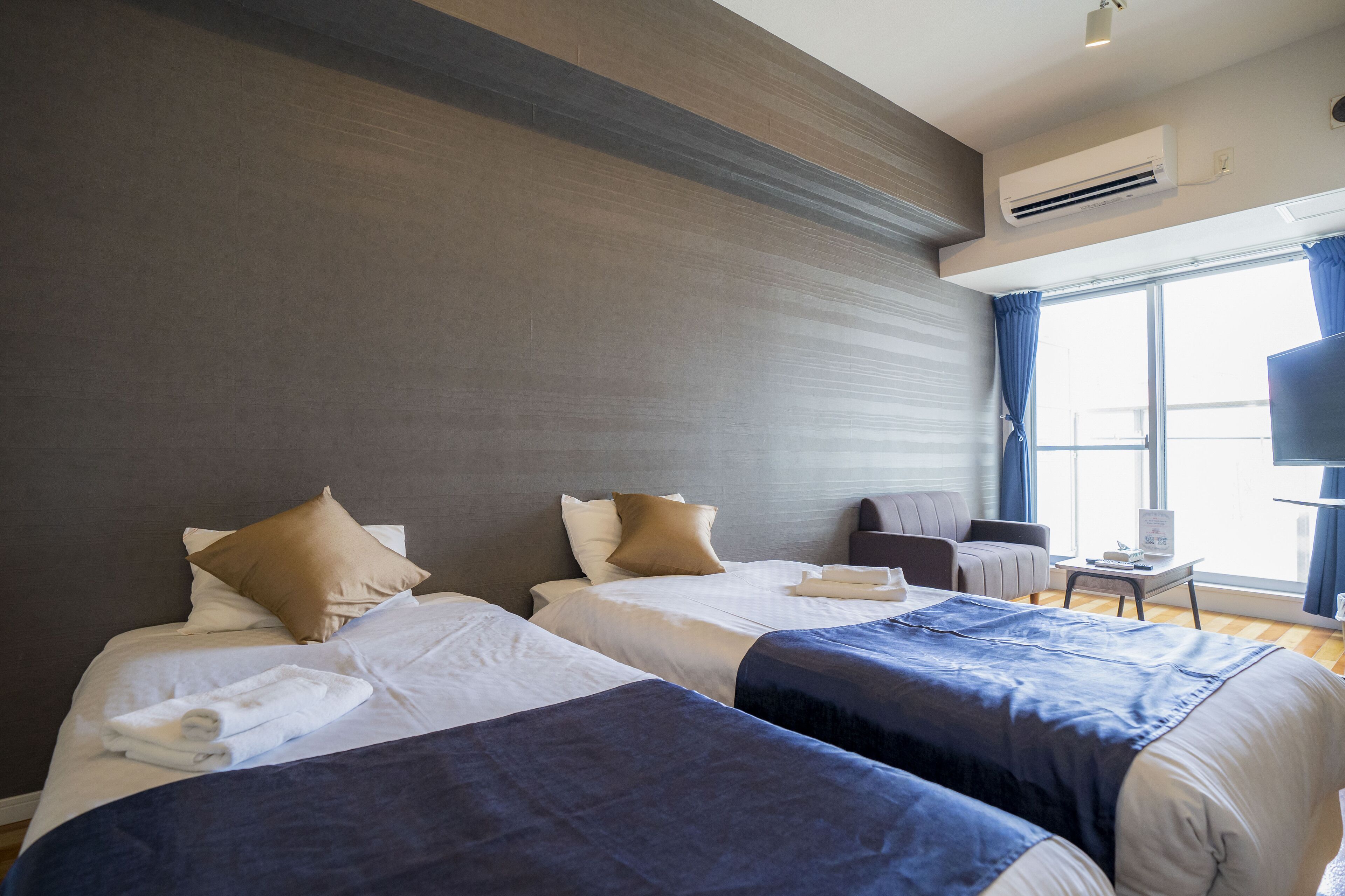 Habitación de hotel con dos camas, un escritorio, una silla y un televisor.