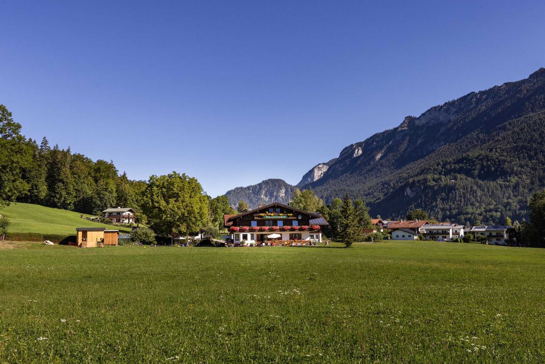 A mountain lodge with a large open field in front, surrounded by forested hills and mountains.