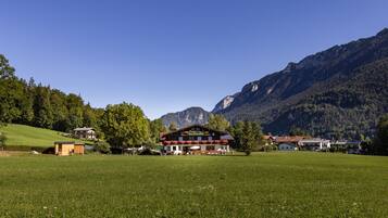 A mountain lodge with a large open field in front, surrounded by forested hills and mountains.