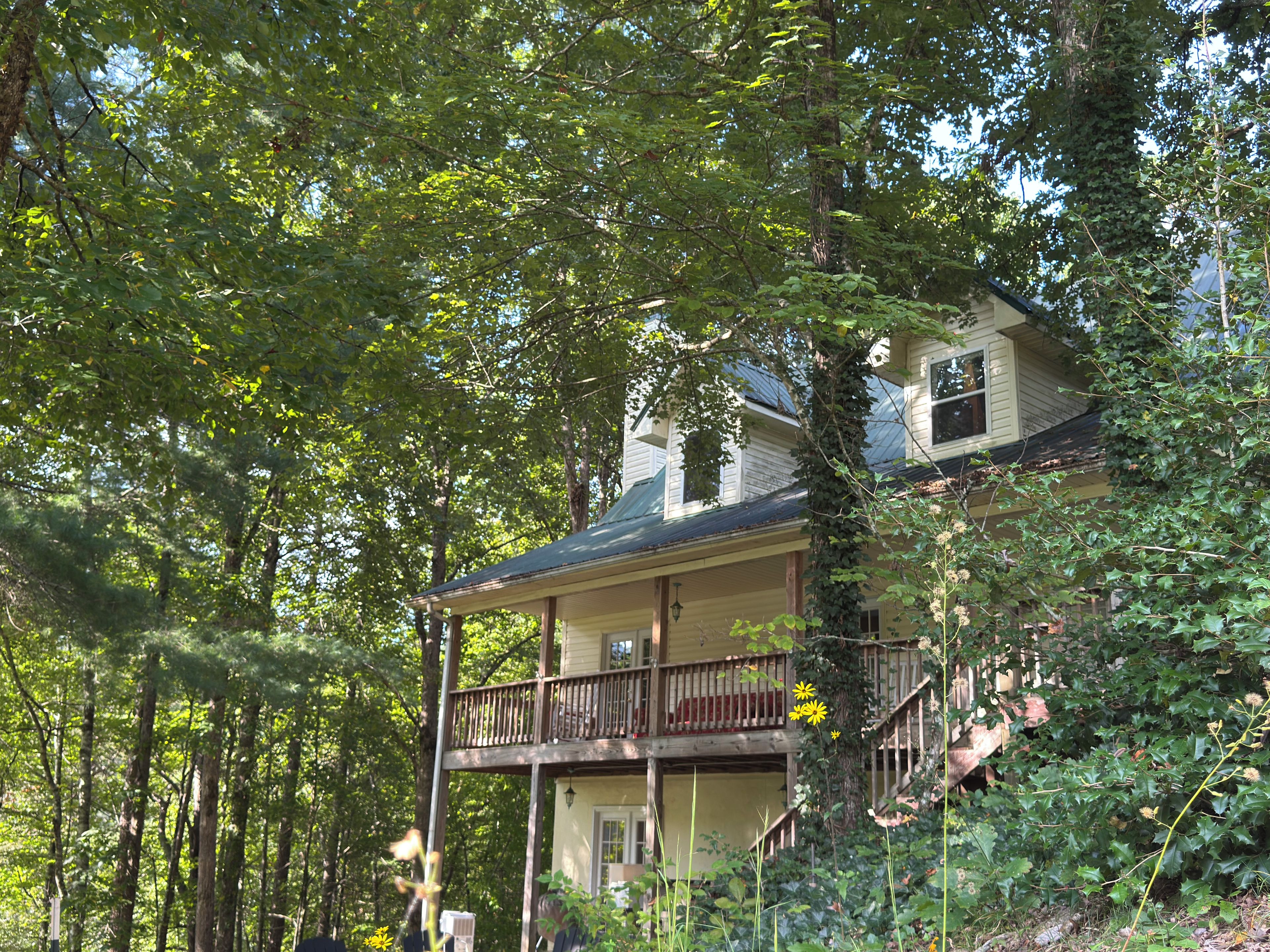 A two-story house with a balcony, surrounded by dense foliage.