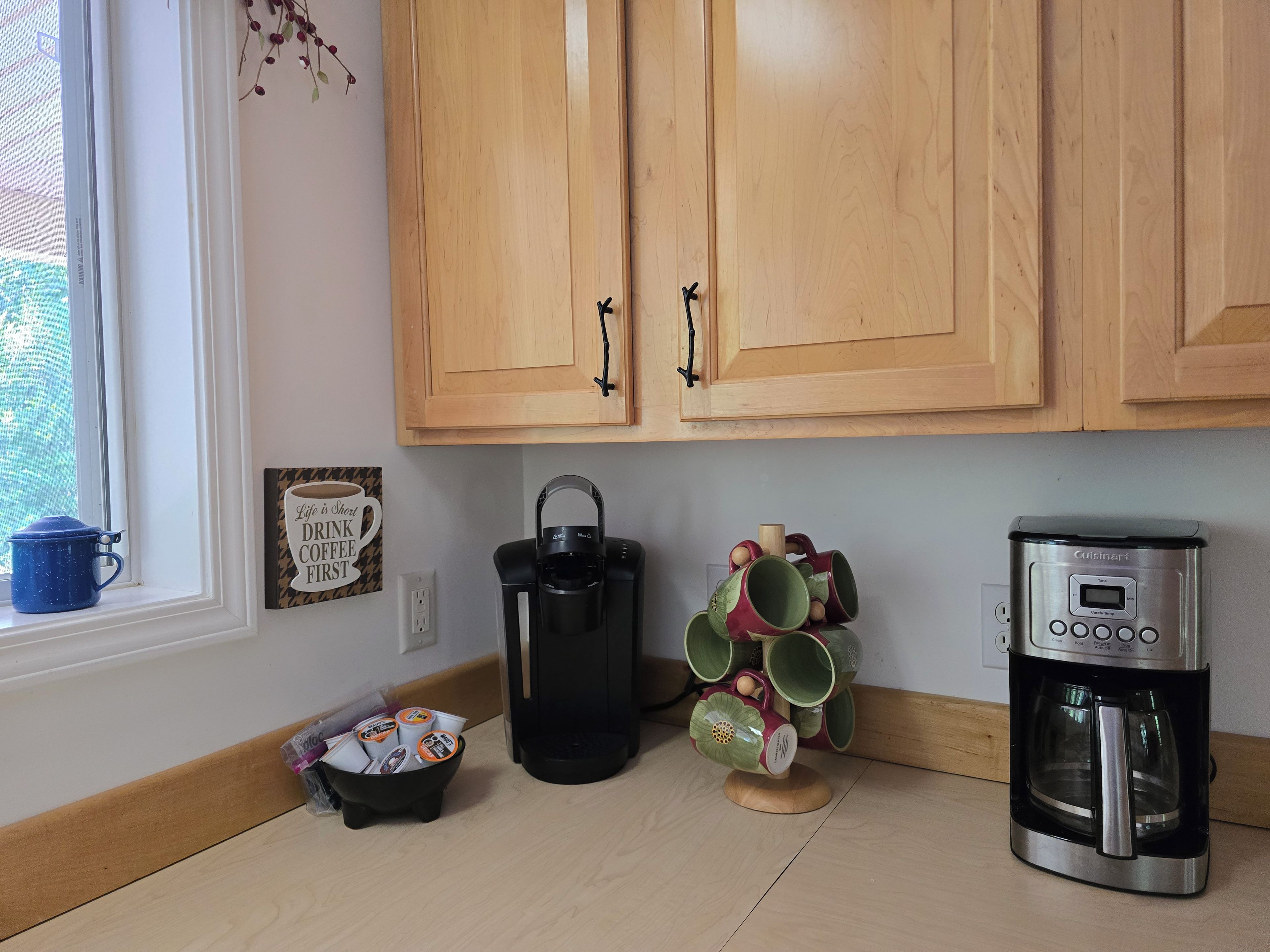A kitchen with wooden cabinets, a coffee maker, a kettle, and a mug holder.