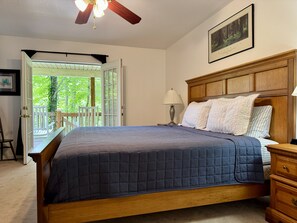A bedroom with a large bed, a nightstand, a wooden headboard, a ceiling fan, and a view of the outdoors. - Mallard Cove - Lakeside (Almond)