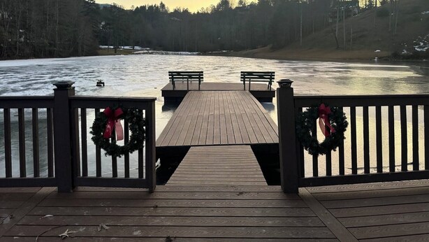 Een houten terras met banken en een leuning, met uitzicht op een rivier met bomen aan weerszijden.