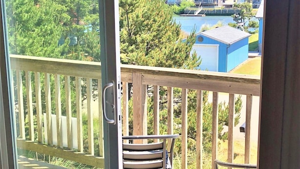 Un balcón con baranda de madera, dos sillas de metal y vista a un lago con casas al fondo.