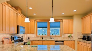 Una cocina con armarios de madera, encimeras de granito, una isla central con taburetes de bar e iluminación colgante.