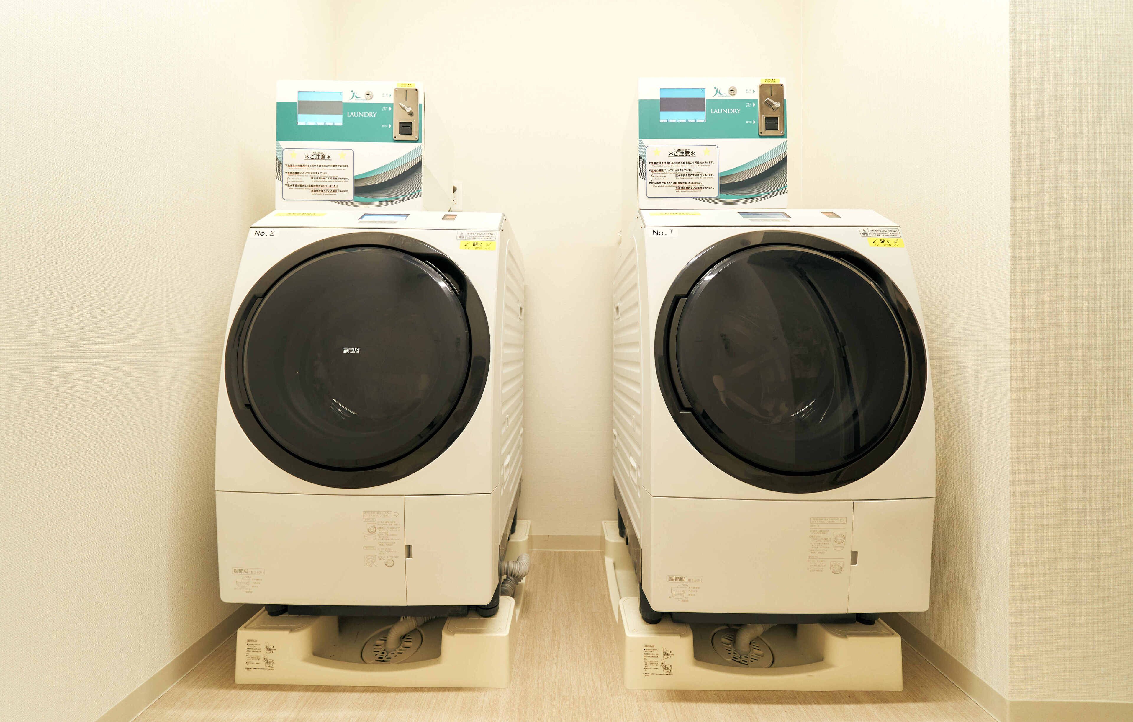 Two front-loading washing machines in a laundry room with control panels on top.