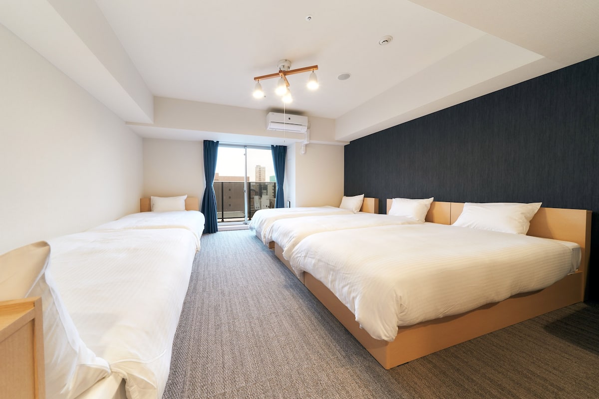 A hotel room with two beds, a large window with curtains, a ceiling light fixture, and an air conditioning unit.