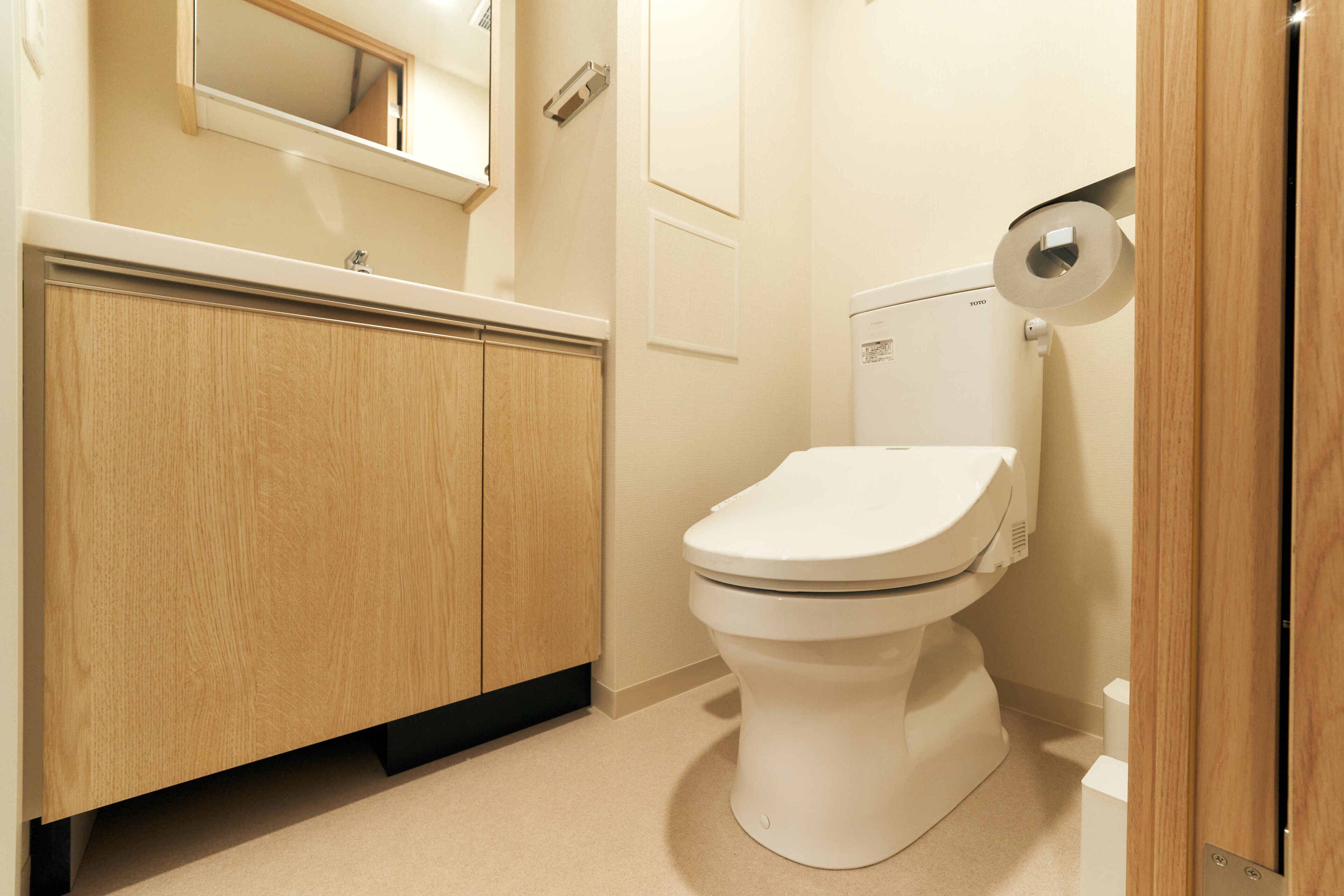 A bathroom with a toilet, wooden cabinets, a mirror, and a toilet paper holder.