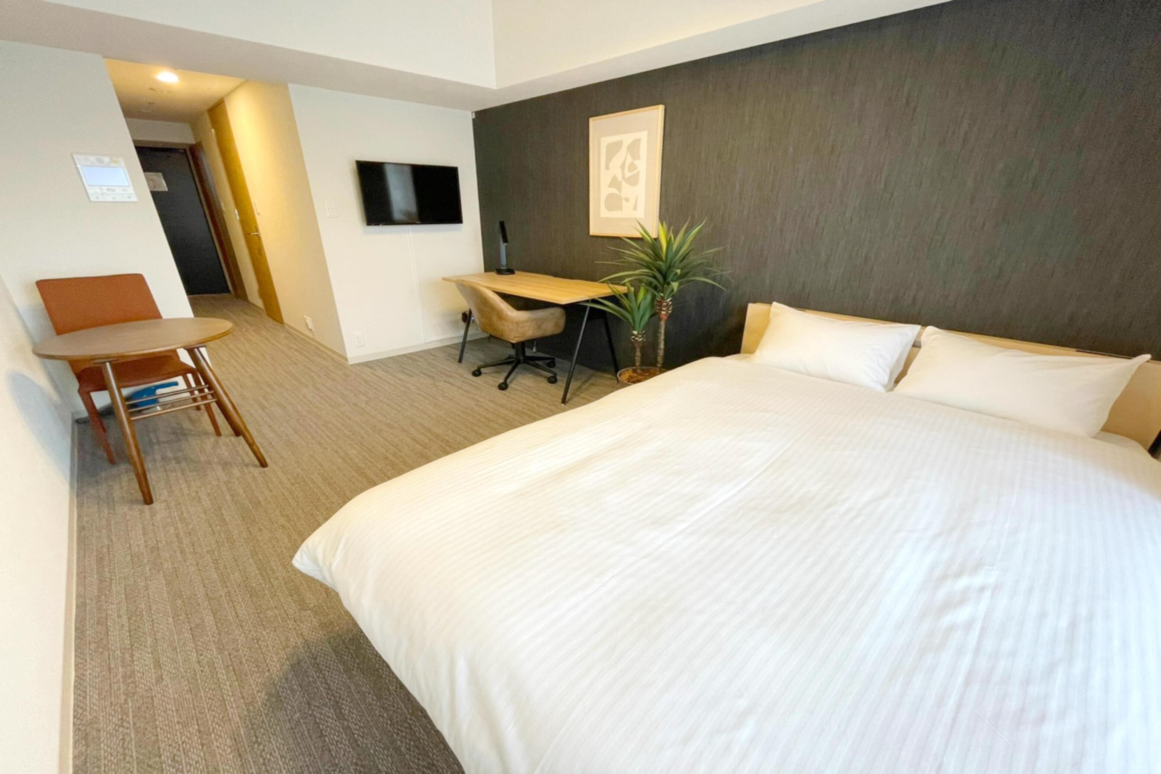 A hotel room with a large bed, a desk, a chair, a television, and a plant.