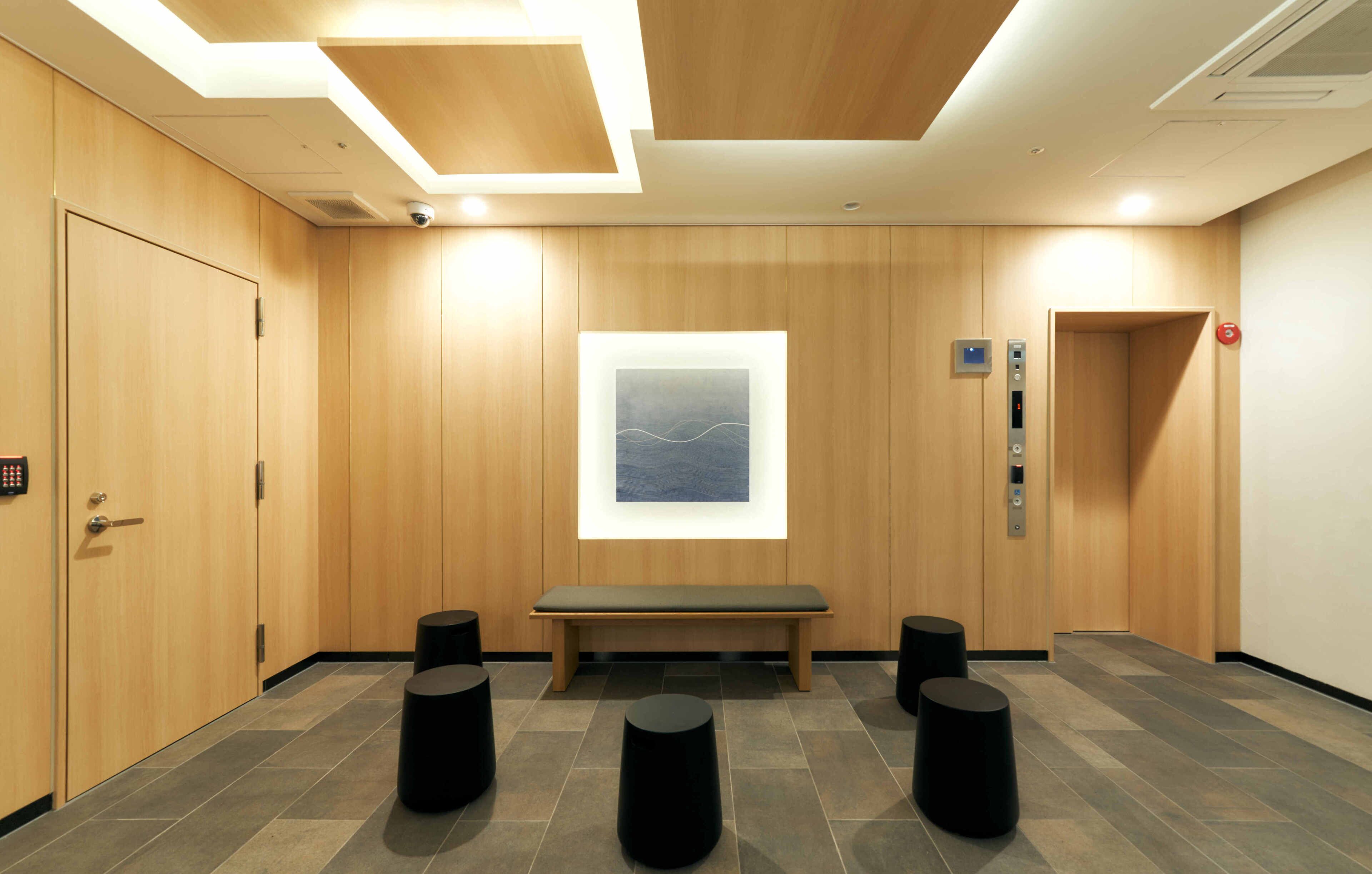 A modern elevator area with a bench, black stools, and a wall-mounted artwork.