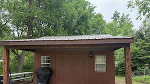 A small wooden cabin with a metal roof, a bench, a grill, and a gravel ground. - Cottonwood Cabin - Cozy Retreat w/ Fire Pit & 150 Acres (Gridley)