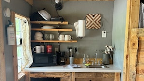 A compact kitchen with wooden cabinetry, a dishwasher, a coffee maker, and a sink. - Cottonwood Cabin - Cozy Retreat w/ Fire Pit & 150 Acres (Gridley)