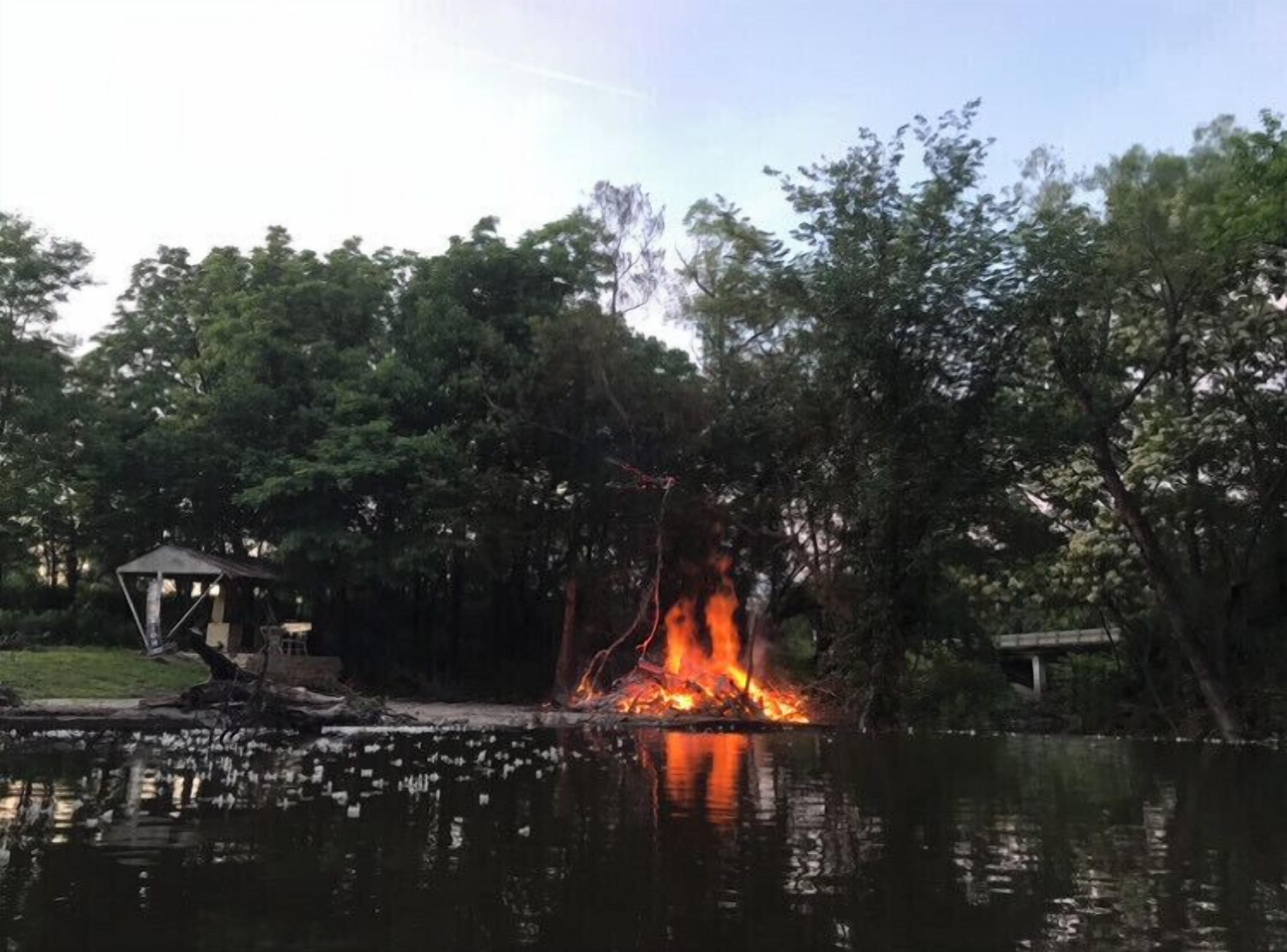Nuotio järven rannalla, taustalla puita ja vasemmalla pieni rakennelma.