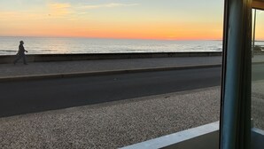 Vista del mar al atardecer desde un paseo cubierto con un camino empedrado y un peatón.