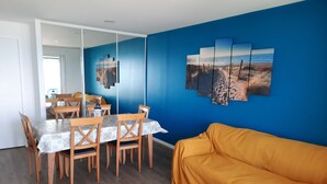 Un área de comedor con una mesa y sillas, un sofá, y una pared con una pintura de playa.