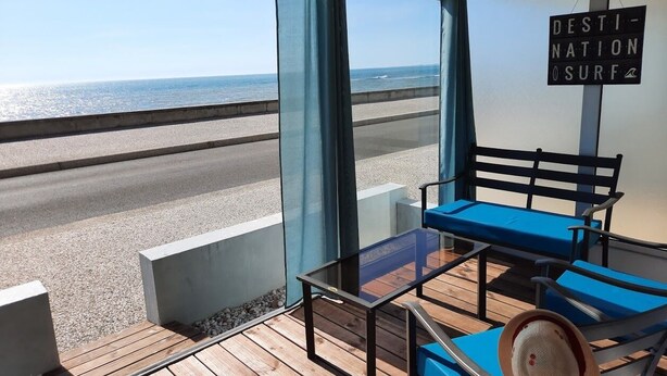 Un balcón con vista a la playa, una silla azul y una mesa.