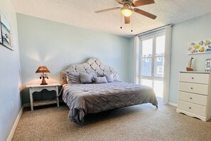 Une chambre à coucher avec un lit, une table de chevet, une lampe, une commode et un ventilateur de plafond.