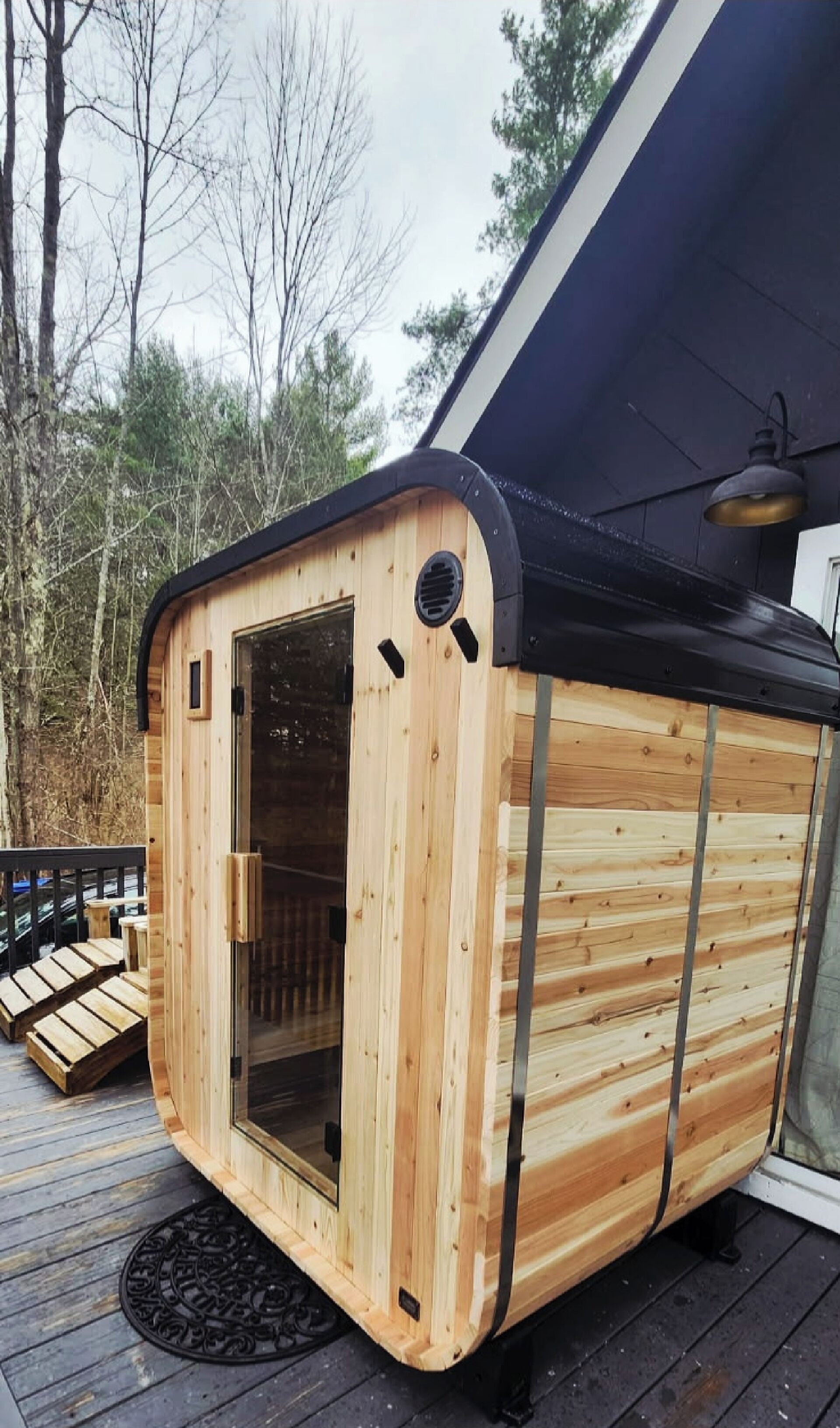 Una cabaña de madera con puerta de vidrio, una terraza y techo negro.