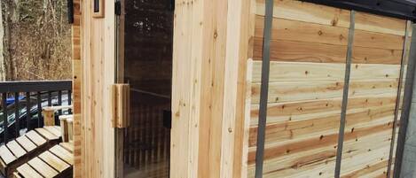 Una cabaña de madera con puerta de vidrio, una terraza y techo negro.