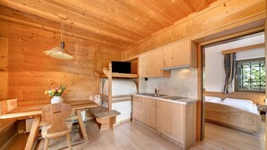 Interno di una baita in legno con tavolo da pranzo, una panca, angolo cottura e un letto.