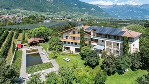 Un moderno edificio a più piani con un impianto di pannelli solari sul tetto, circondato da vegetazione lussureggiante e montagne sullo sfondo.