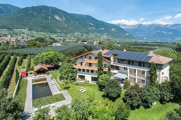 Un moderno edificio a più piani con un impianto di pannelli solari sul tetto, circondato da vegetazione lussureggiante e montagne sullo sfondo.