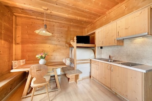 Interno di una baita in legno con angolo cottura, zona pranzo e una panca.