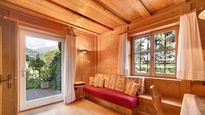 Un interno in legno con un divano, una poltrona, una finestra con tende e vista su un'area verde.