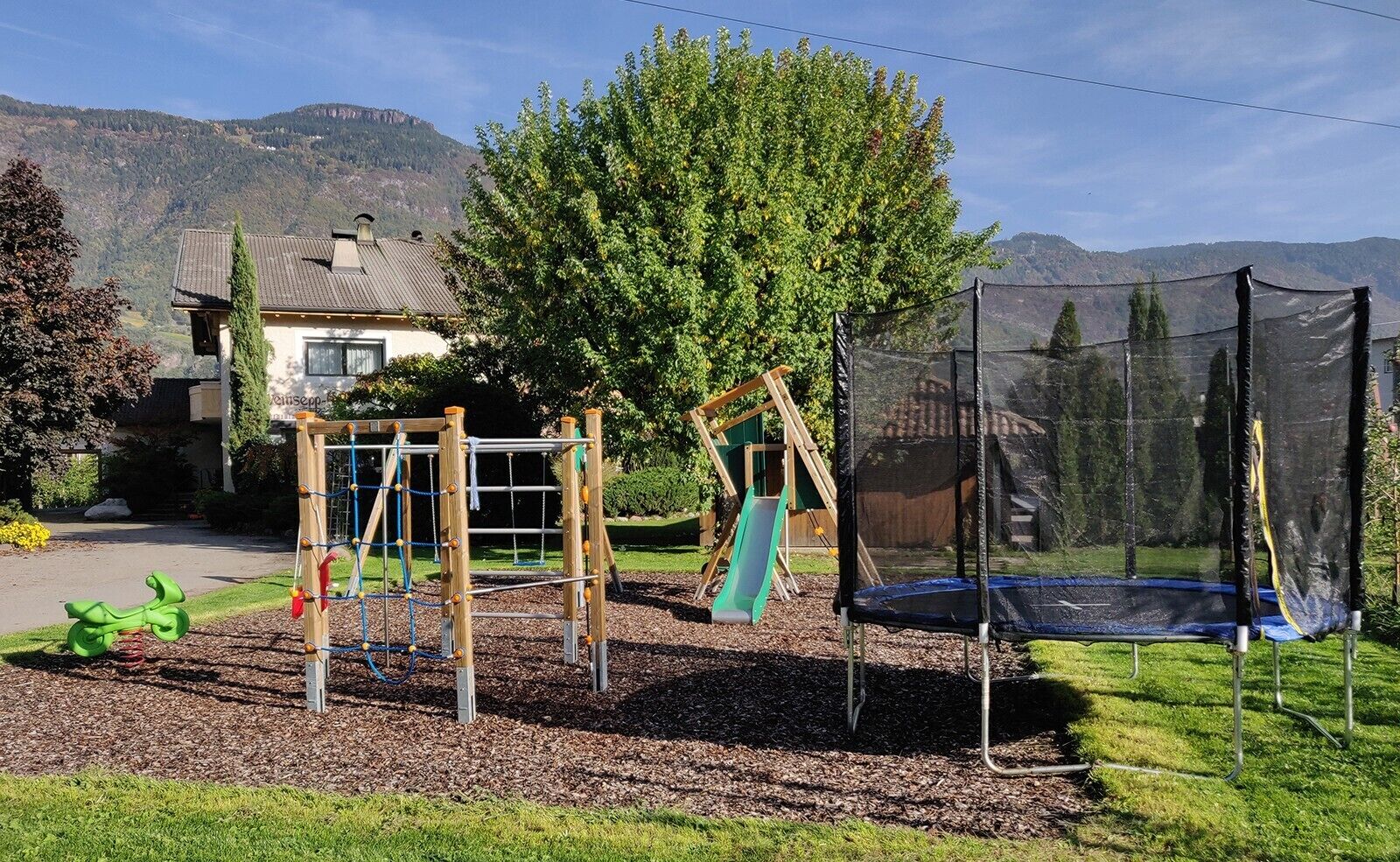 Ein Spielplatz mit Schaukel, Rutsche und Trampolin.